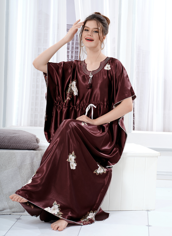 Model sitting wearing brown satin kaftan for women with white floral print and drawstring waist