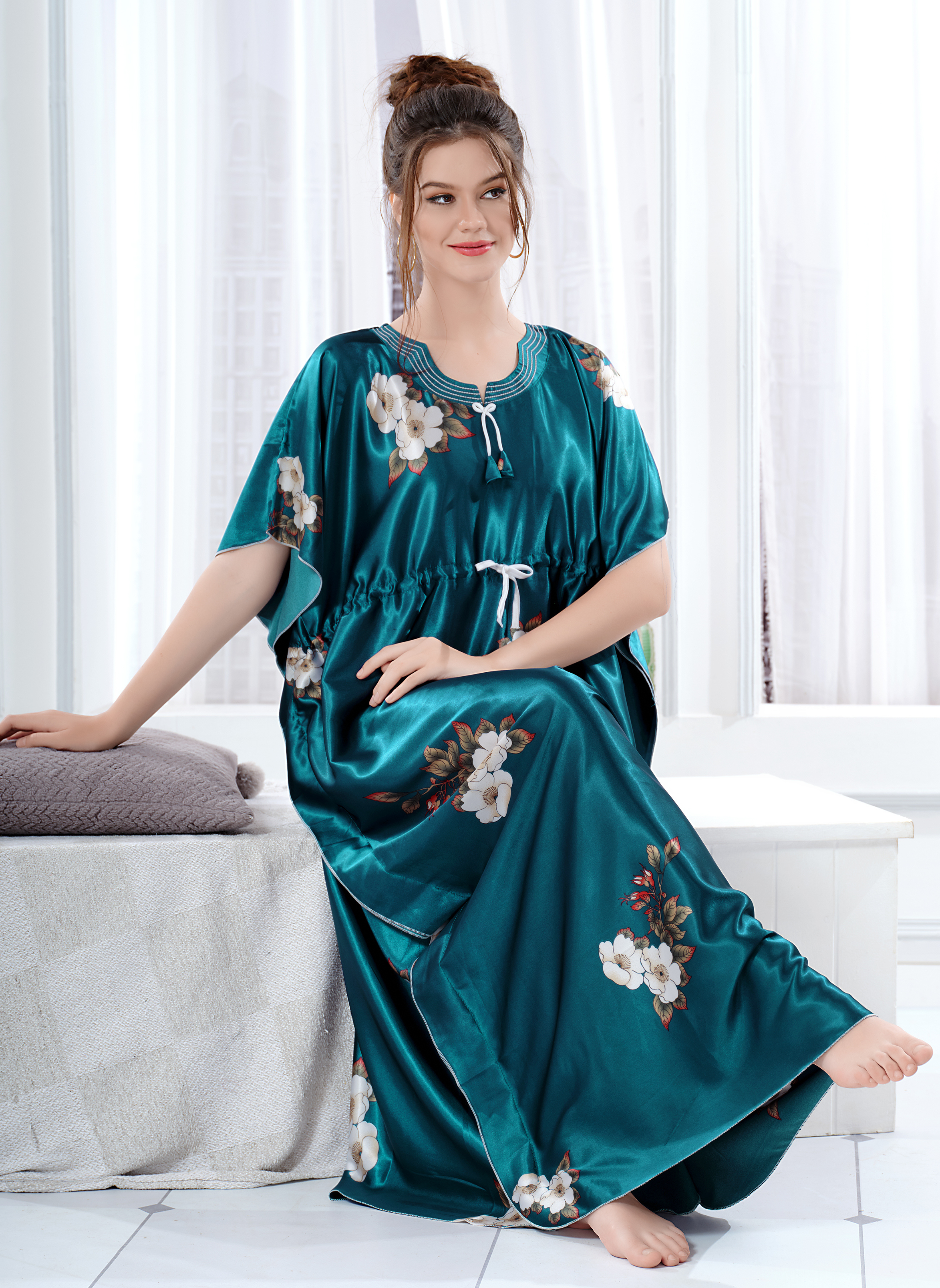 Model sitting wearing teal green satin kaftan for women with white floral print and drawstring waist