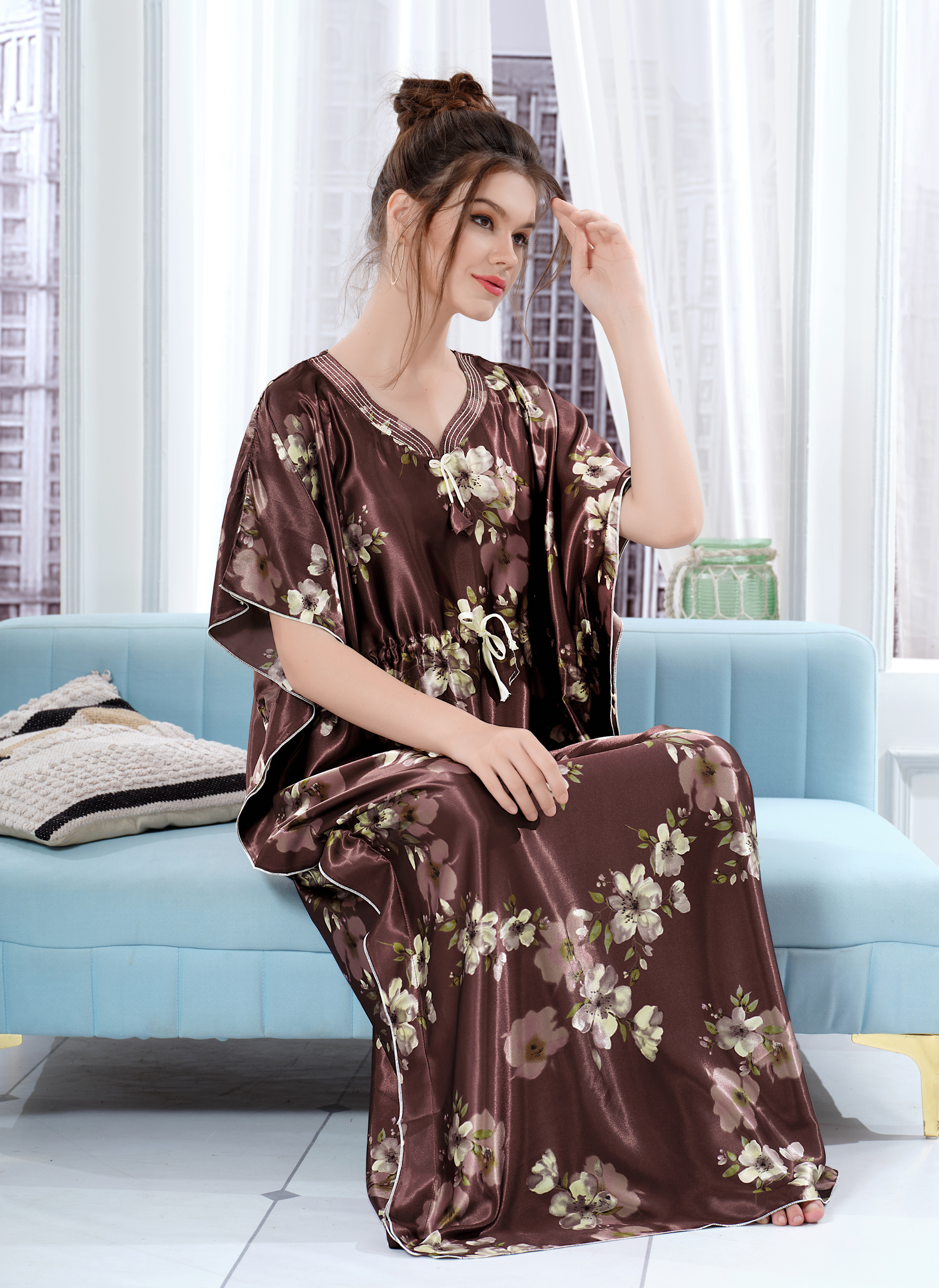 Model sitting on sofa wearing chocolate brown satin kaftan for women with floral print and drawstring waist