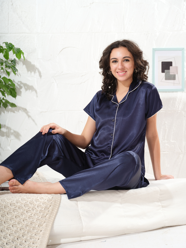 Model sitting wearing navy blue solid satin night suit for women with short sleeves and white piping