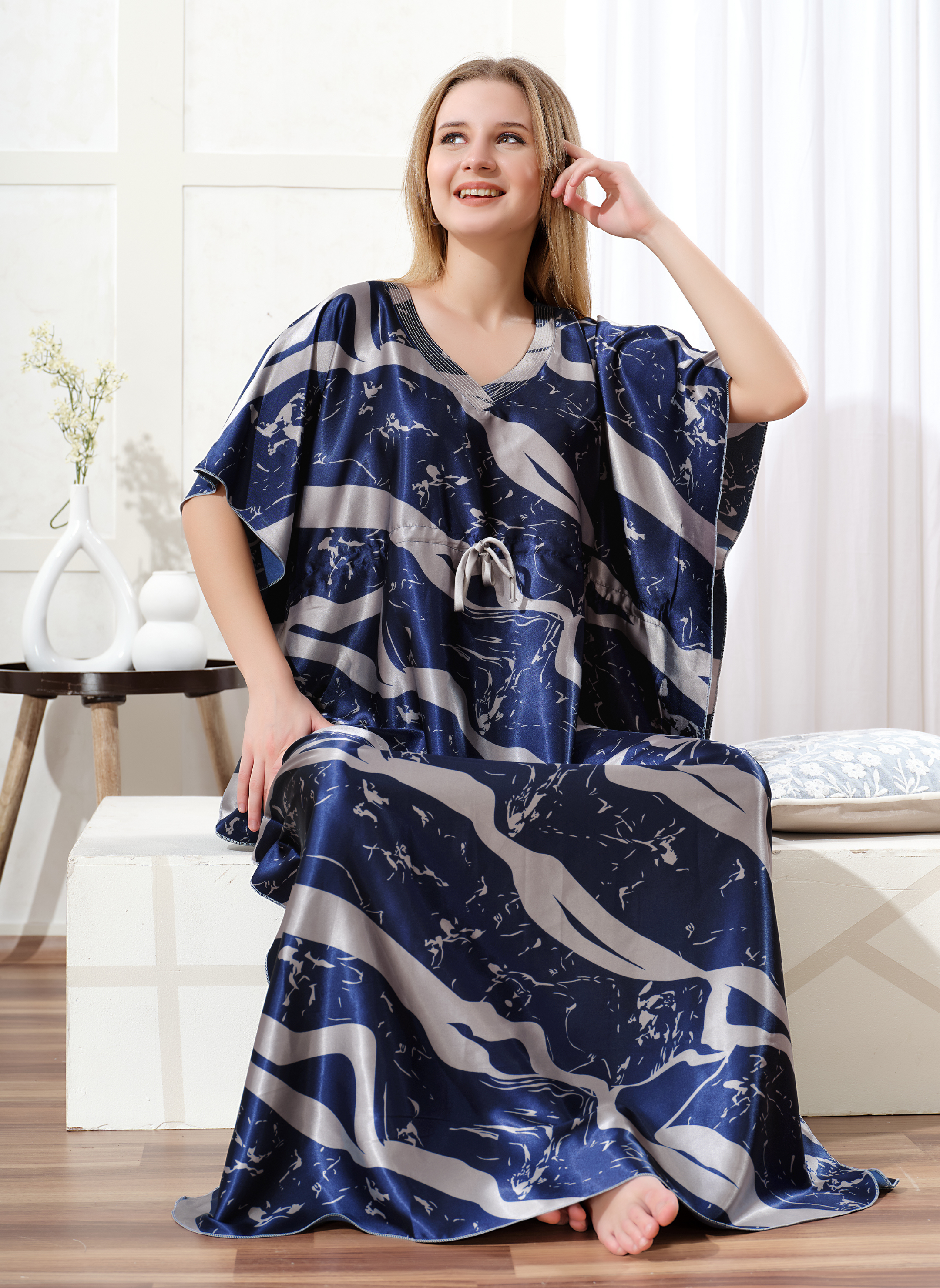 Model sitting wearing dark blue satin kaftan for women with silver abstract print and drawstring waist