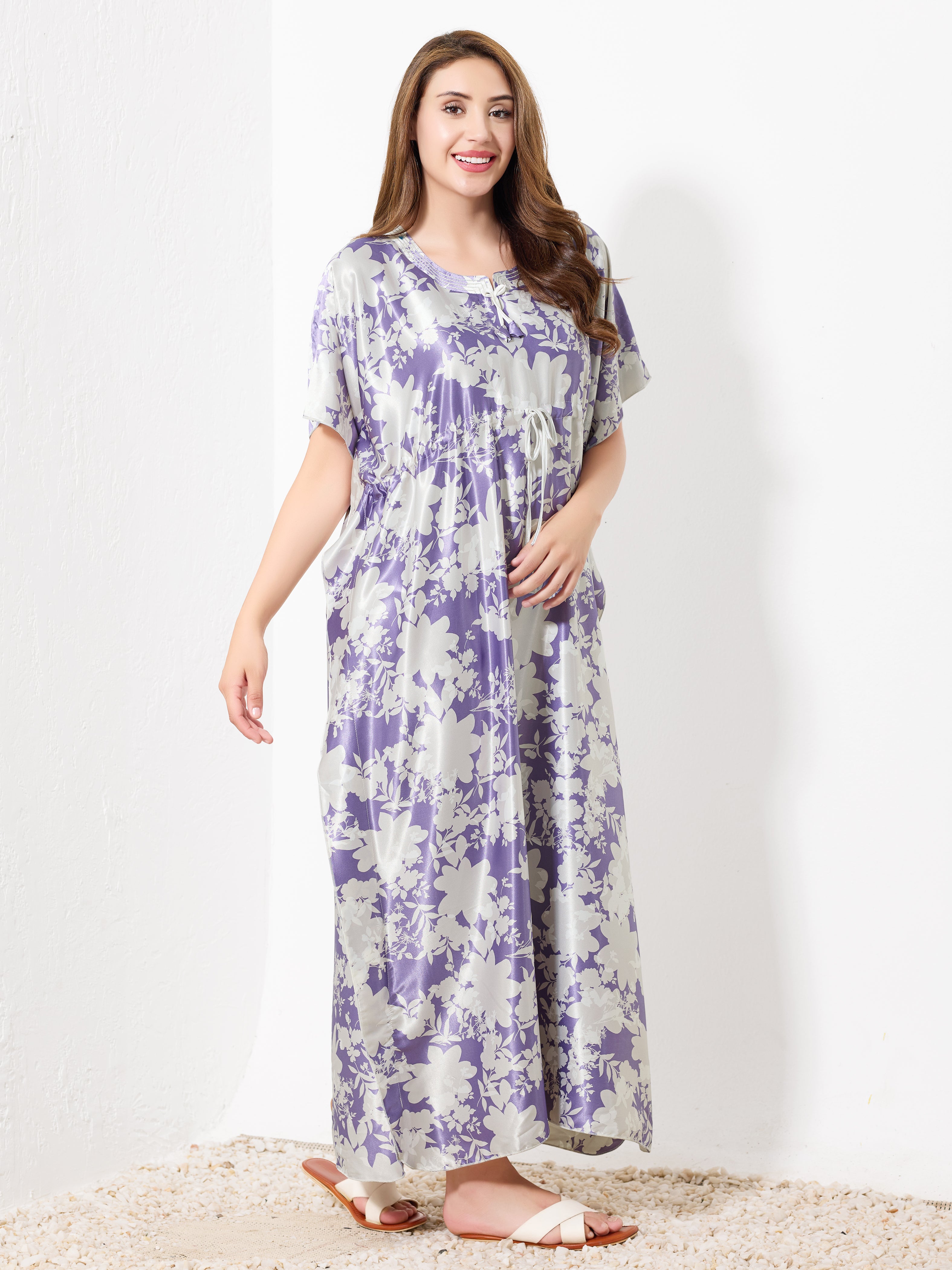 A woman with long brown hair wears the Priincezz Nightwear Purple & White Floral Kaftan as elegant loungewear, paired with white sandals, standing and smiling against a plain white background.